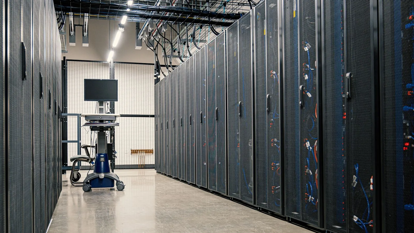 Aisle of black server cabinets in a data center with cable trays running overhead